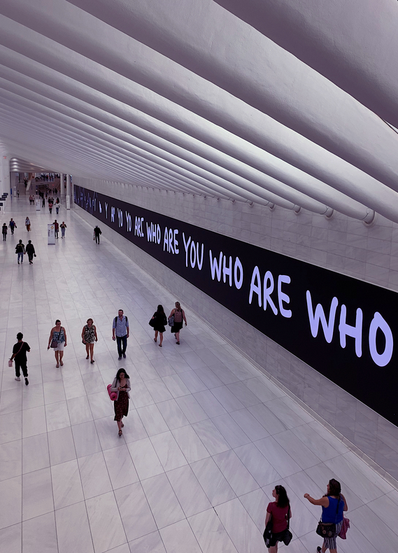Foto eines Bahnhofs mit Menschen, an der Wand der Schriftzug "WHO ARE YOU"