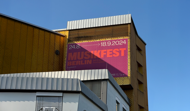 Großes Plakat zum Musikfest Berlin 2024 an der Fassade der Berliner Philharmonie, mit den Terminen 24. August bis 18. September 2024 auf violett-rotem Hintergrund.