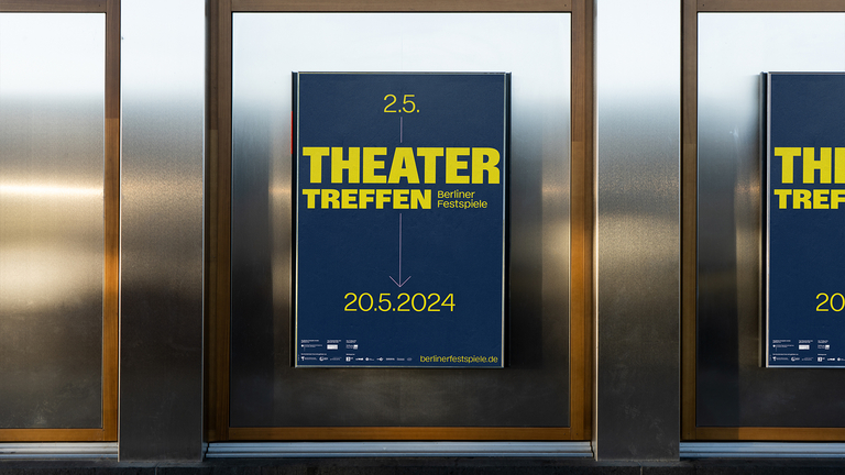 Nahaufnahme eines Ausstellungsplakats für das Theatertreffen 2024 (2. bis 20. Mai). Das Design zeigt gelbe Typografie auf dunkelblauem Grund und ist in einem hochwertigen Metallrahmen zwischen Holzleisten montiert.