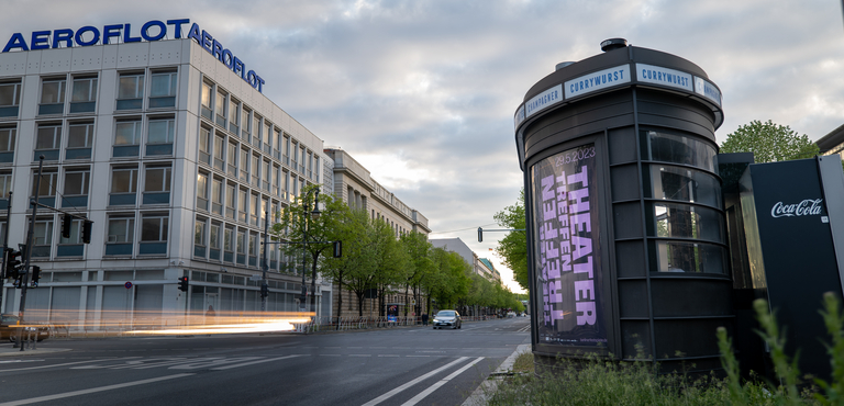 Berliner Straßenszene Unter den Linden mit einer Litfaßsäule im Vordergrund, die ein Plakat des Theatertreffens zeigt.