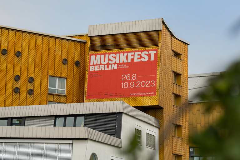 Großes orangenes Plakat zum Musikfest Berlin 2023 an der Fassade der Berliner Philharmonie mit Festivaldatum 26. August bis 18. September 2023.