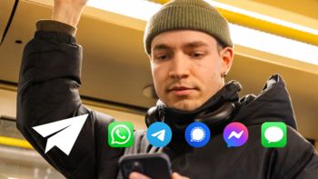 Ein junger Mann mit grüner Mütze und schwarzen Kopfhörern um den Hals steht in einer U-Bahn. Er hält sich mit einer Hand an einer gelben Haltestange fest und blickt konzentriert auf sein Smartphone in der anderen Hand. Auf dem Bild sind Symbole verschiedener Messenger-Apps überlagert, darunter WhatsApp, Telegram, Signal, Facebook Messenger und iMessage, was auf digitale Kommunikation und mobile Vernetzung hindeutet.