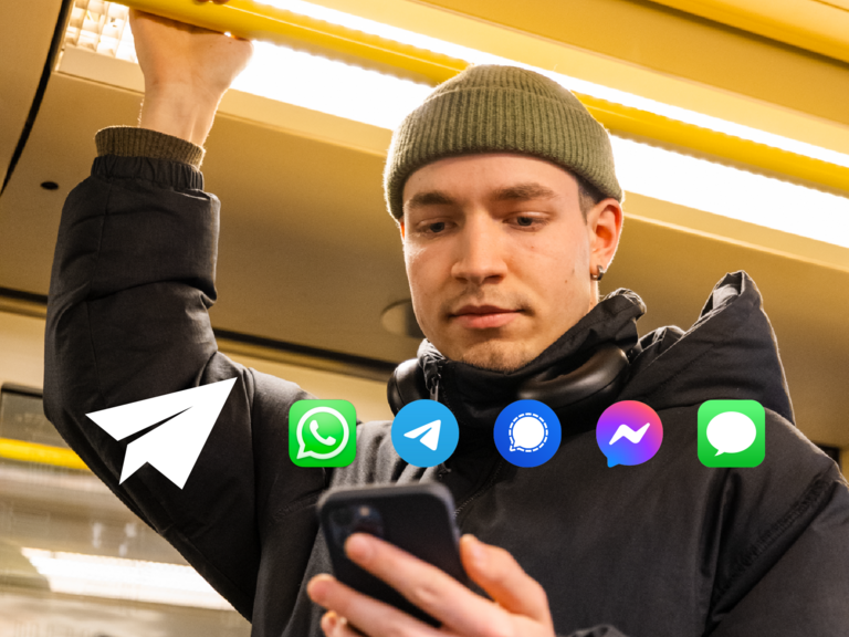 Ein junger Mann mit grüner Mütze und schwarzen Kopfhörern um den Hals steht in einer U-Bahn. Er hält sich mit einer Hand an einer gelben Haltestange fest und blickt konzentriert auf sein Smartphone in der anderen Hand. Auf dem Bild sind Symbole verschiedener Messenger-Apps überlagert, darunter WhatsApp, Telegram, Signal, Facebook Messenger und iMessage, was auf digitale Kommunikation und mobile Vernetzung hindeutet.
