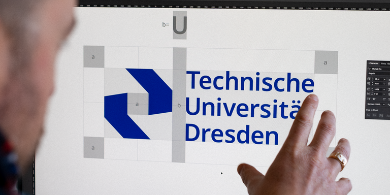Eine Person sitzt vor einem Bildschirm und zeigt auf das Logo der Technischen Universität Dresden