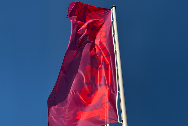 Violett-rote Fahne mit Schriftzug Musikfest Berlin, wehend an einem Fahnenmast vor blauem Himmel.